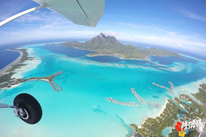 Aerial view of a tropical island with turquoise waters and bungalows, seen from a plane.
