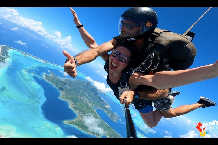 Two people tandem skydiving over a tropical island with blue ocean and clear skies.