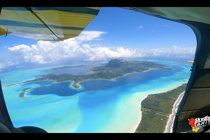 View from plane of a tropical island surrounded by turquoise water and clouds.