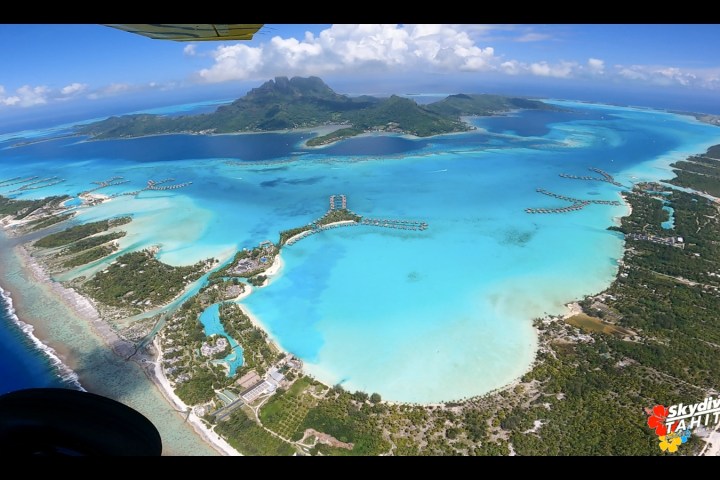Aerial view of tropical island and turquoise lagoon with distant mountains.