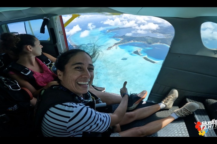 Two people in a plane above turquoise waters, one giving a thumbs up.