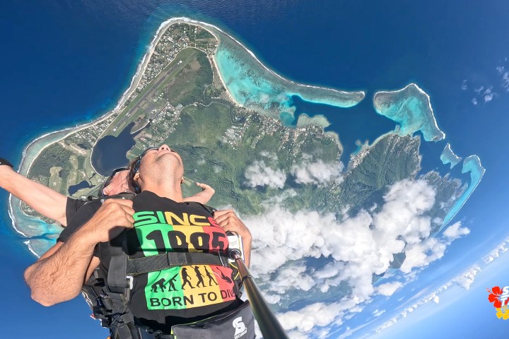 Tandem skydive over tropical island with clear blue ocean and clouds.