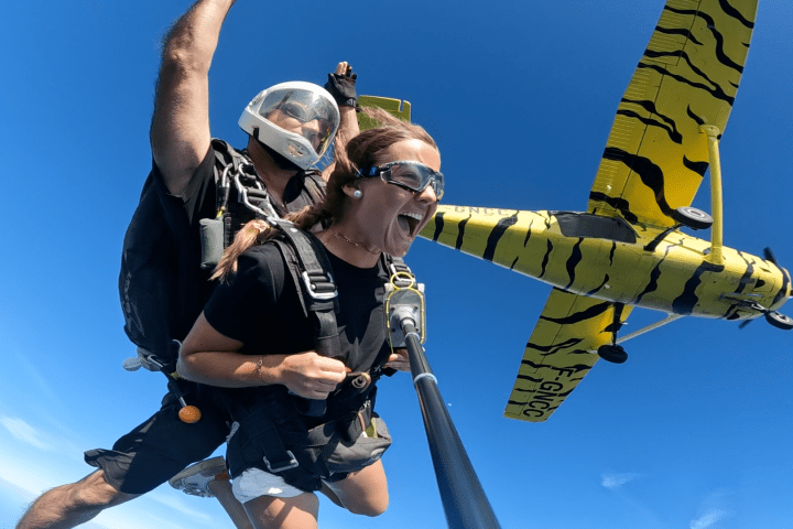 Tandem skydivers near a yellow airplane, with a bright blue sky in the background.