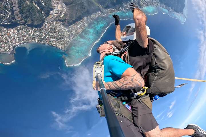 Two people skydiving over coastal landscape with ocean view.
