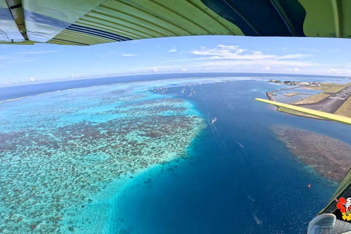 Aerial view of a coast and runway, with clear blue water and coral reefs visible from an airplane window.