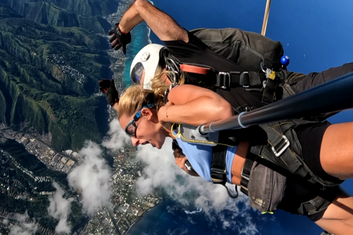 Tandem skydive over Tahiti, showing skydivers, coastline, and ocean, with 'Skydive Tahiti' logo.